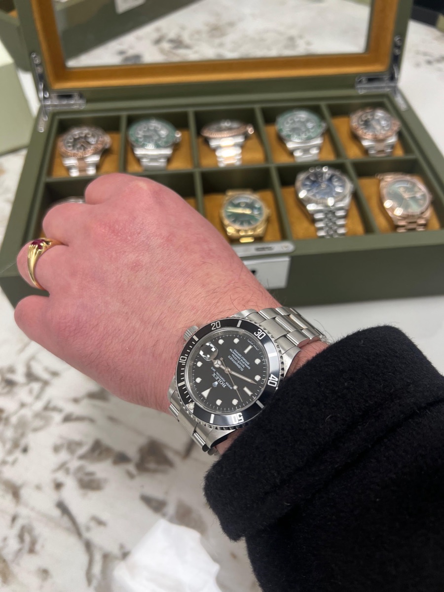 Rolex Submariner worn on the wrist, with a collector's watch case of pieces behind